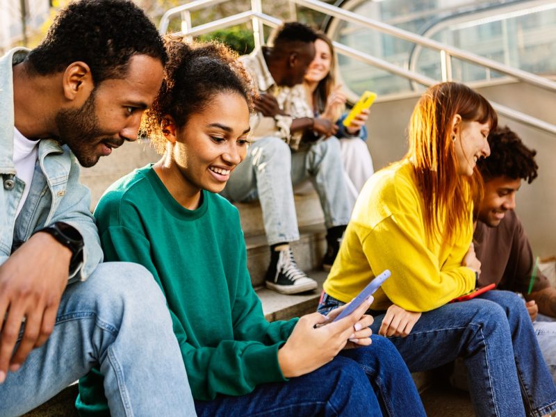 Group of young people using mobile phone sitting at staircase in the city